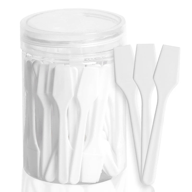 A clear plastic jar filled with small, white plastic cosmetic spatulas, with three spatulas leaning against the jar.