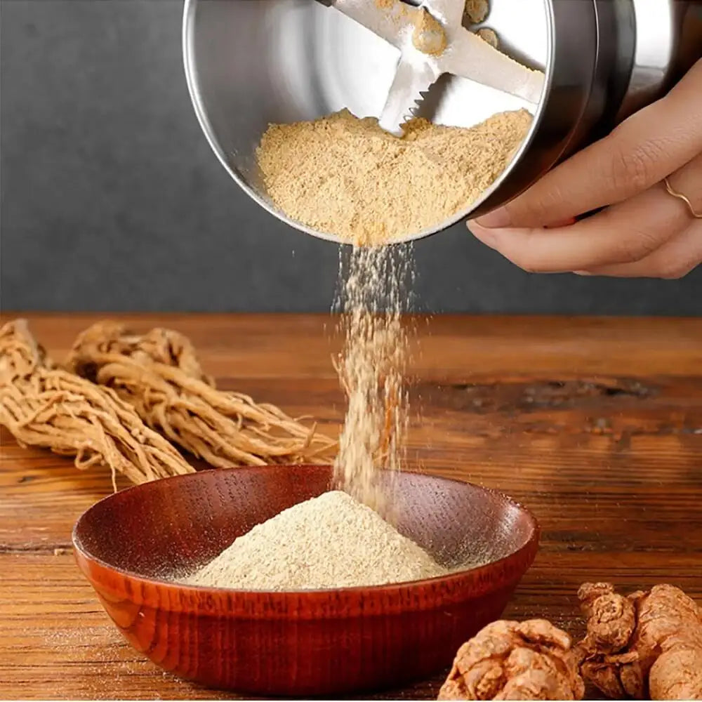 Stainless steel electric spice and herb grinder pouring ground ginseng powder into a small wooden bowl.