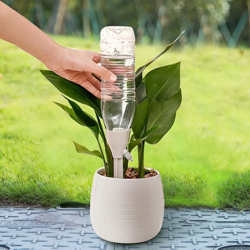 White automatic plant watering device standing in a pot with clear bottle reservoir.