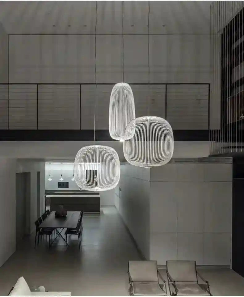 Three spherical and cylindrical white wire cage pendant lights suspended in a modern two-story home interior.