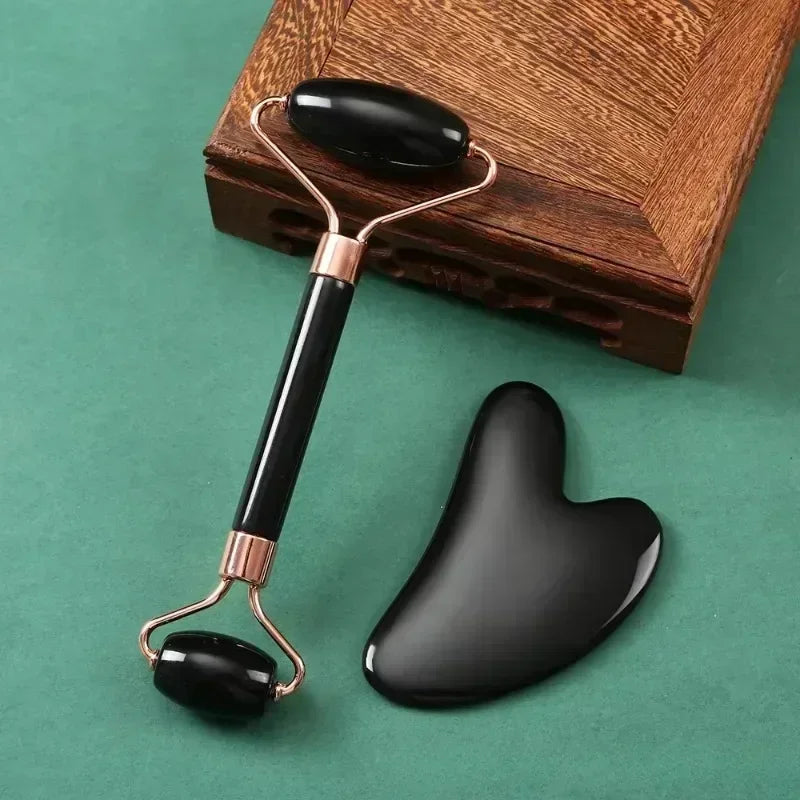 Black resin facial roller and heart-shaped Gua Sha scraper tool set for anti-aging skin massage and face lifting.
