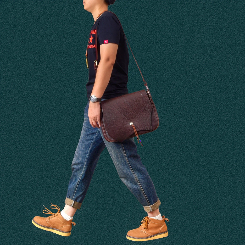 Vintage handmade dark brown cowhide leather messenger bag with flap, brass button closure, and adjustable shoulder strap.