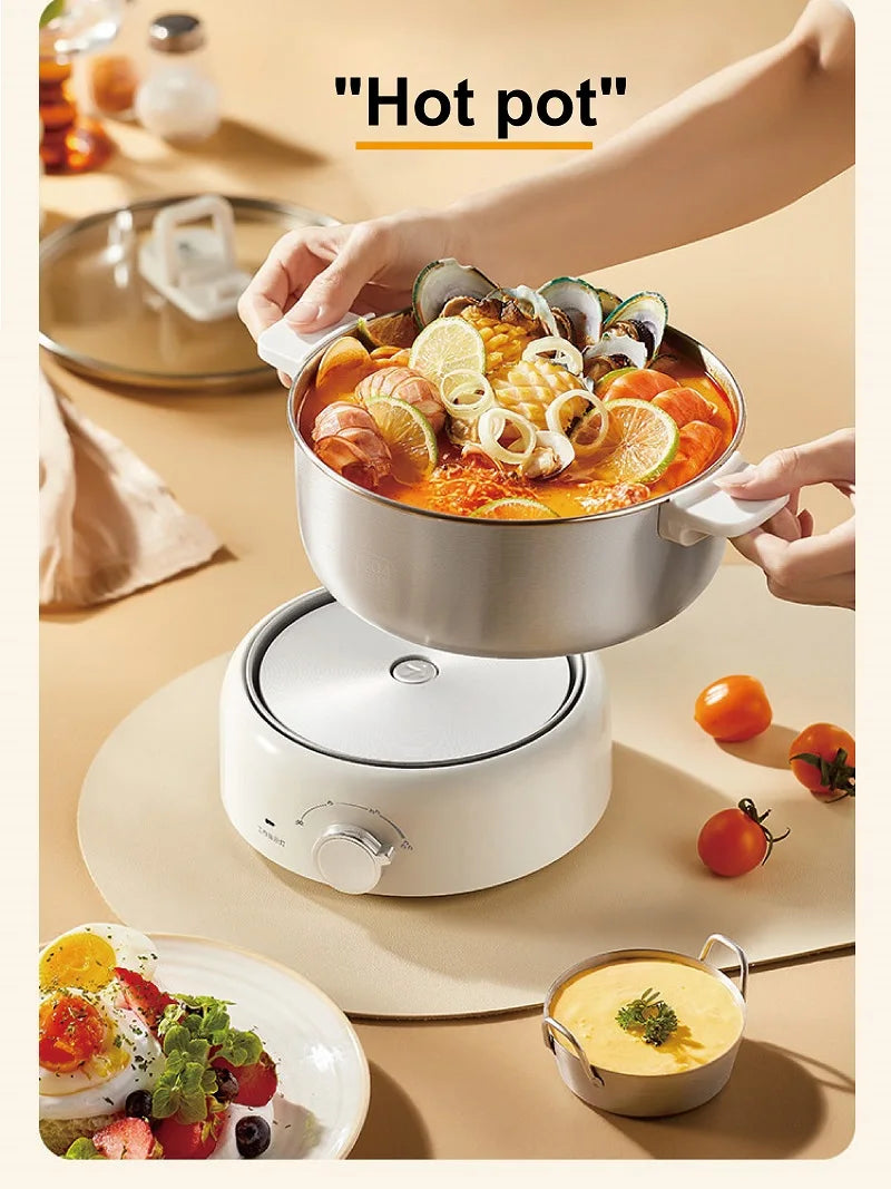 Stainless steel hot pot with lid and side handles filled with soup on a white heater base