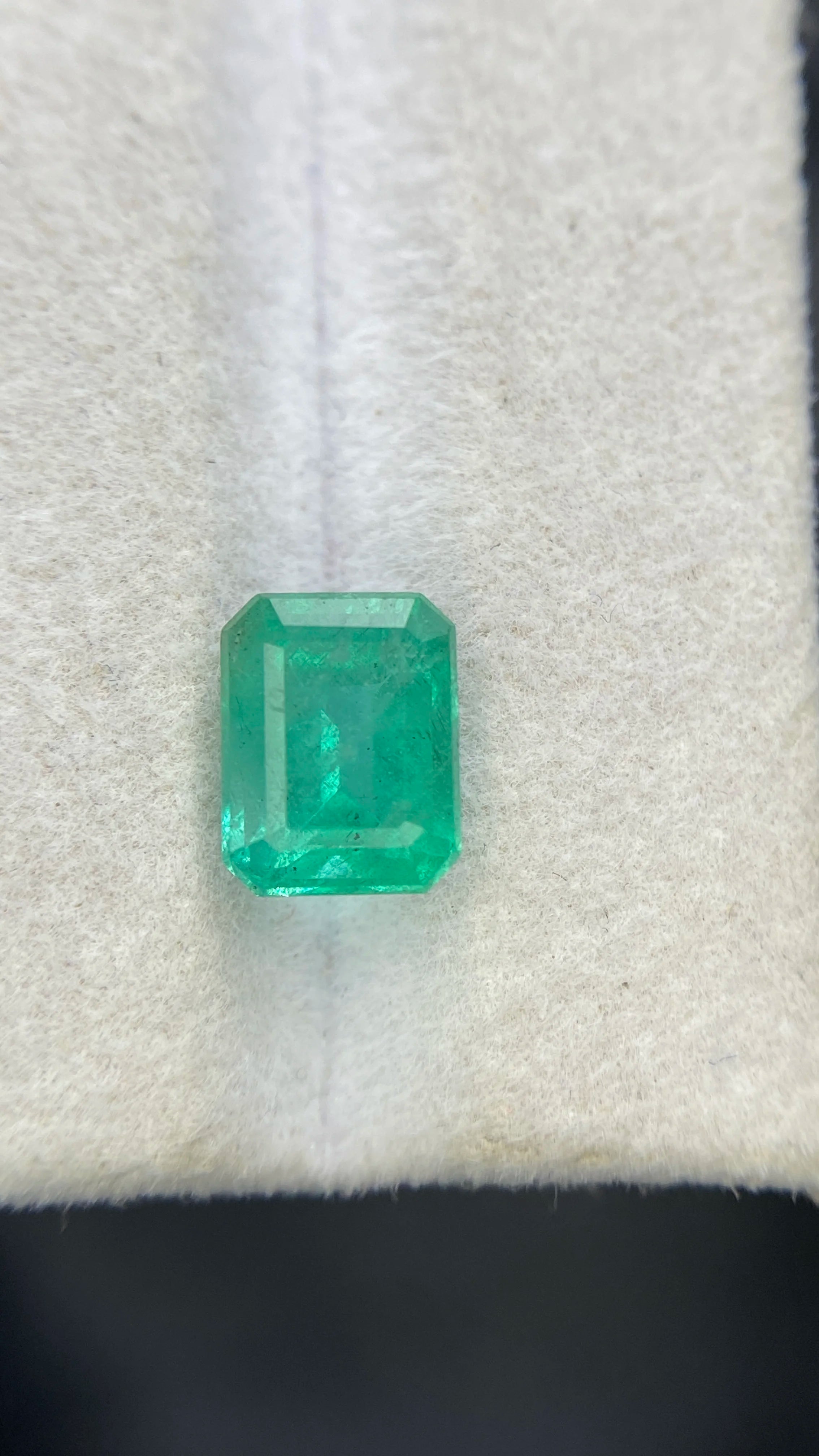 Front view of emerald-cut green gemstone on white felt
