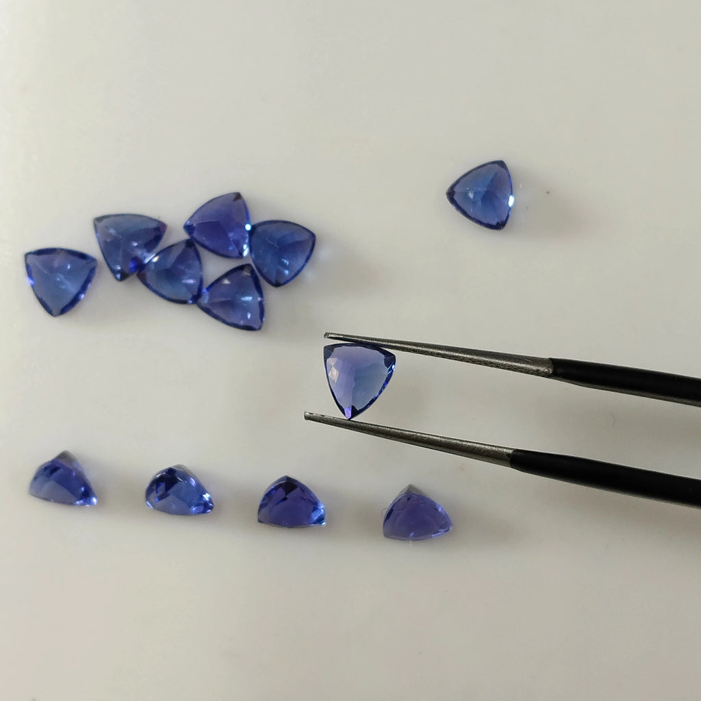 Loose blue trillion-cut gemstones, shown with tweezers holding a triangular gem