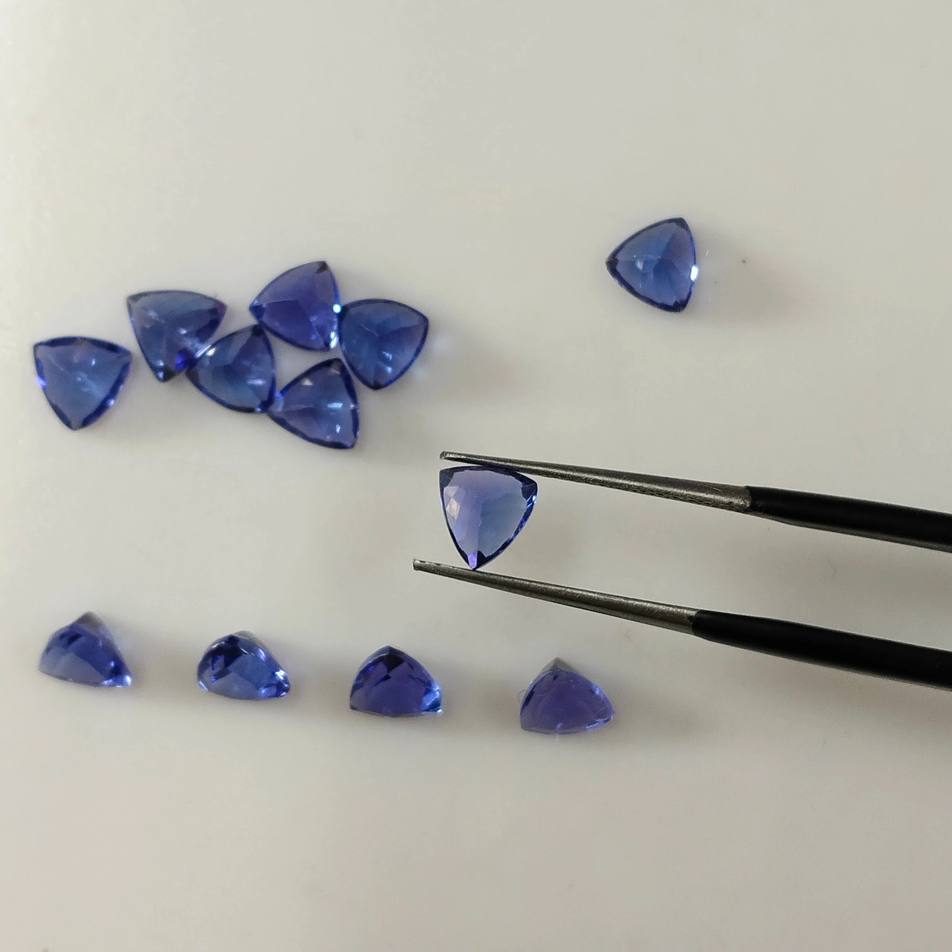 Loose blue trillion-cut gemstones, shown with tweezers holding a triangular gem