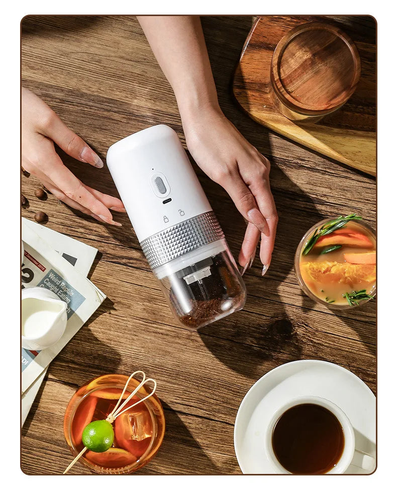 Portable white electric coffee grinder with clear bean hopper and silver metal accent on a wooden table.