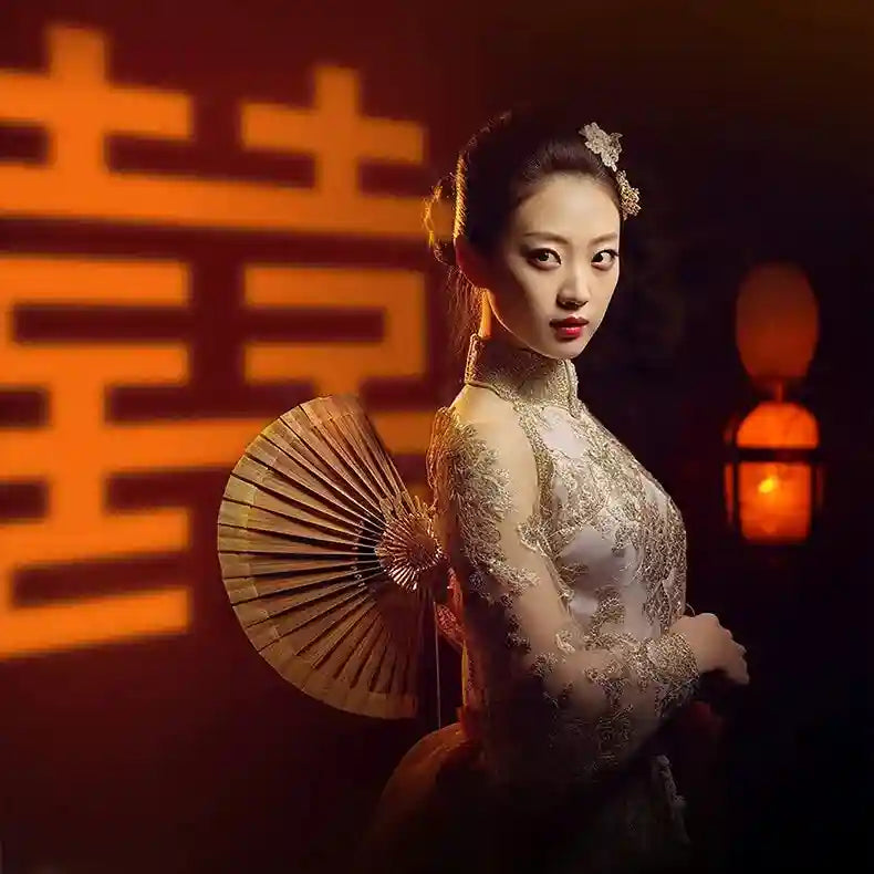 Woman wearing a high-neck, long-sleeved ivory lace cheongsam with gold embroidery, holding a circular wooden hand fan.