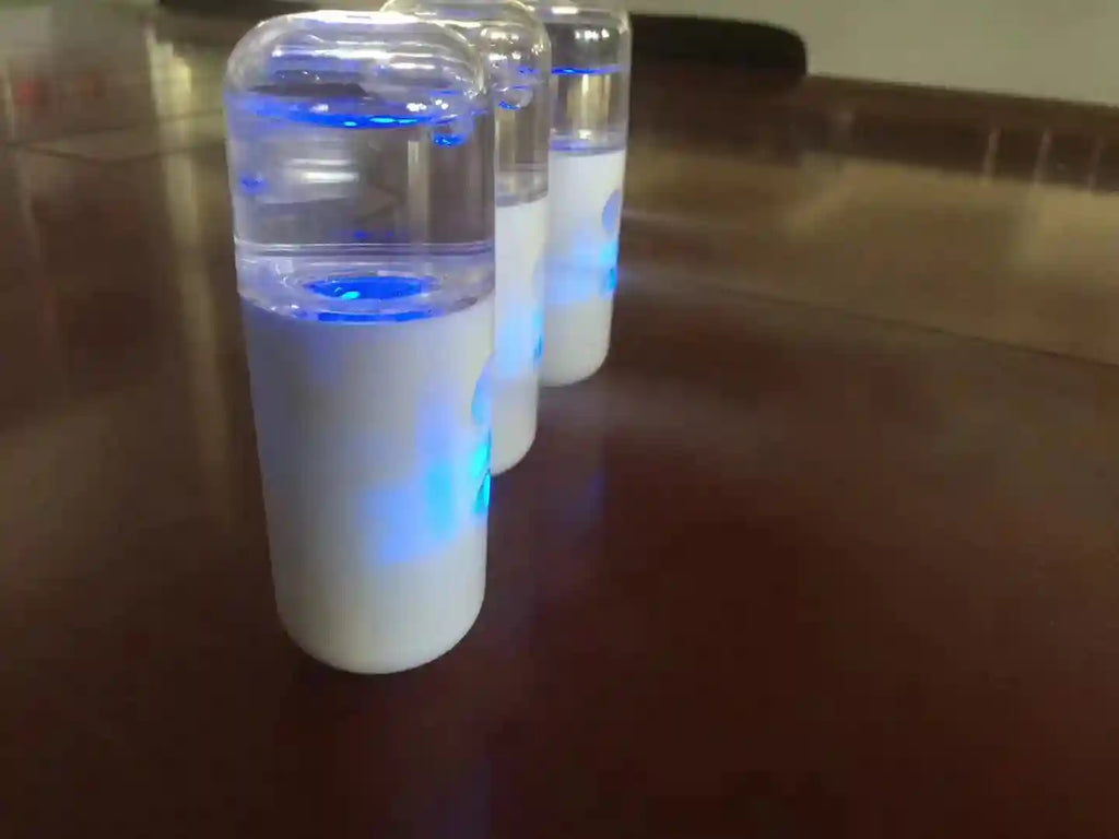Portable white nano facial mister sprayers with blue LED light for face hydration and eyelash care on a table.