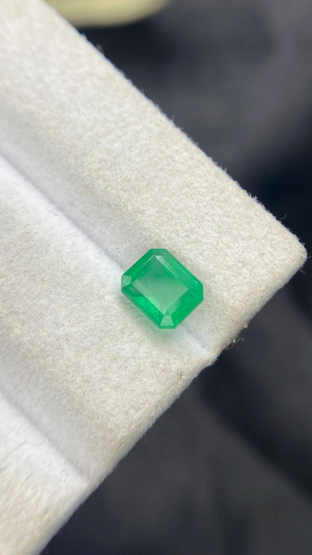 Green emerald-cut gemstone on white pad, angled close-up