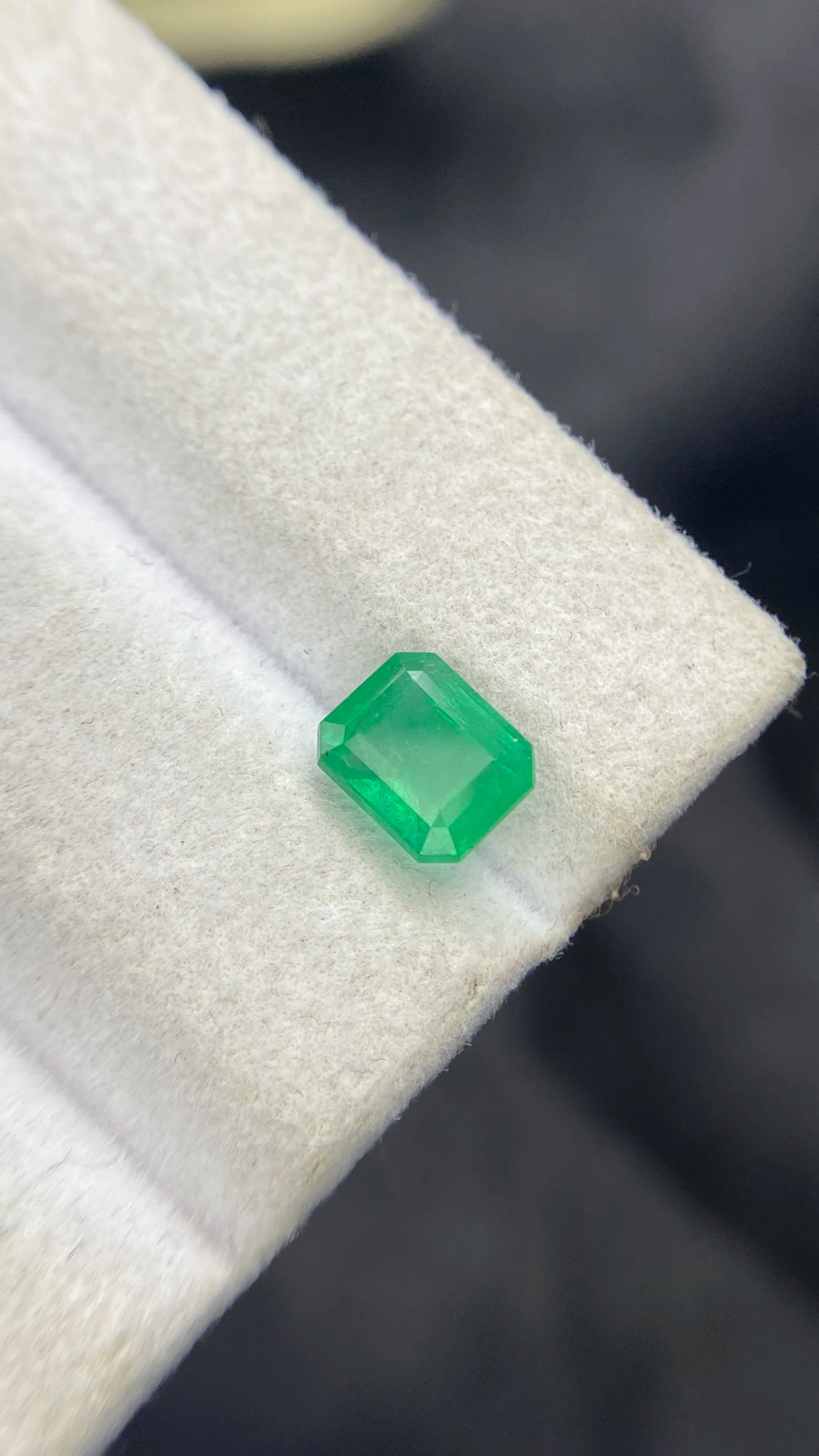 Green emerald-cut gemstone on white pad, angled macro view