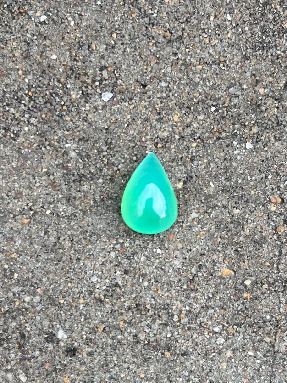 Turquoise-green chrysoprase pear-shaped cabochon gemstone, polished teardrop on gravel.