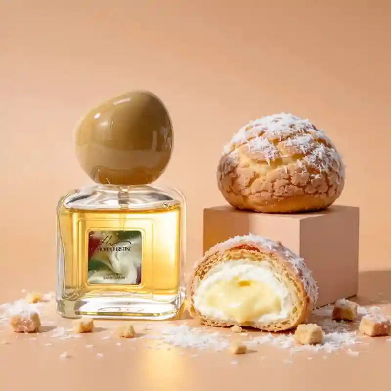 Square glass perfume bottle with a round beige cap, next to a coconut cream puff on a peach-colored background.