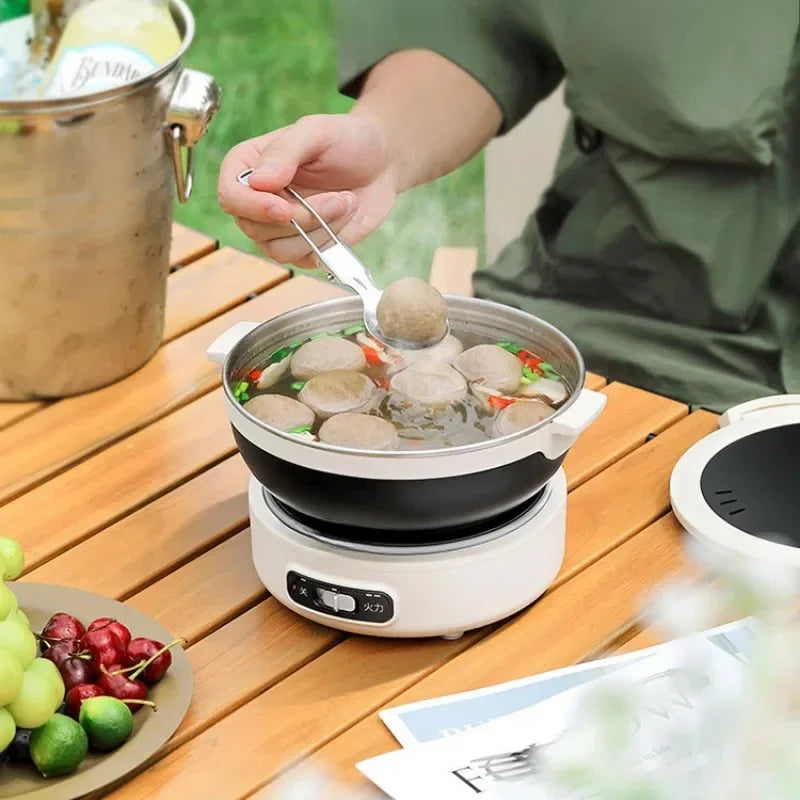 Electric split hot pot cooker with black bowl filled with broth and sliced ingredients