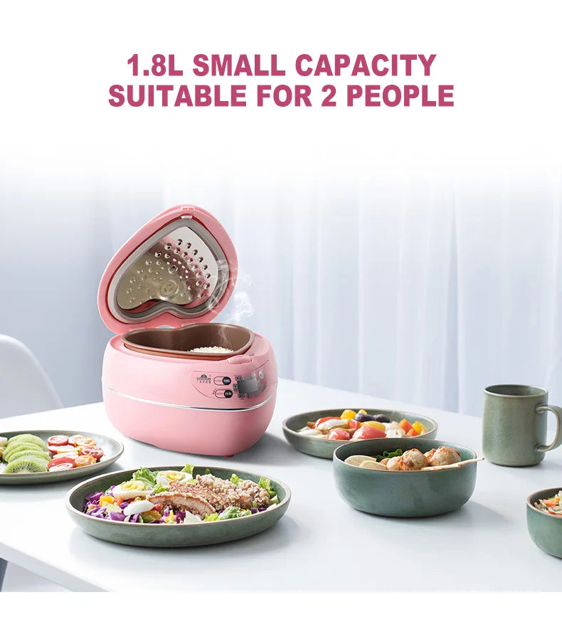 Pink heart-shaped mini rice cooker on a table with small bowls of food nearby.