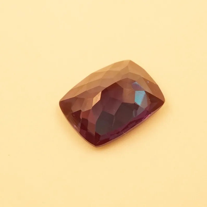 Faceted cushion-cut alexandrite gemstone, dark reddish-brown with faint teal at the center