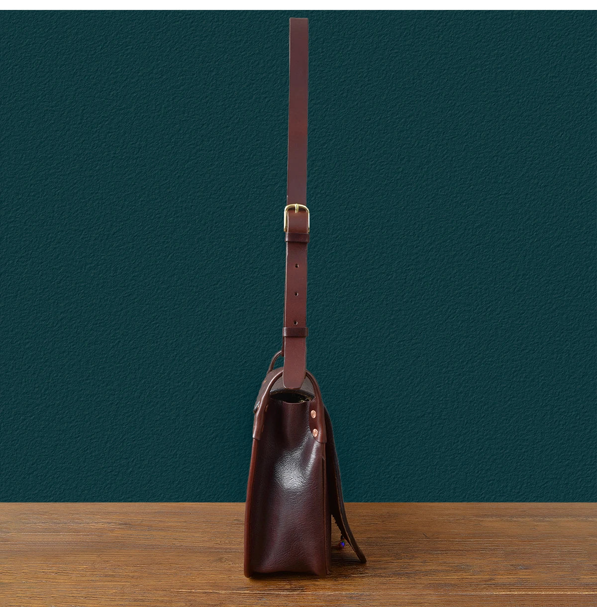 Side view of vintage handmade dark brown cowhide leather messenger bag with adjustable strap, luxury designer style.