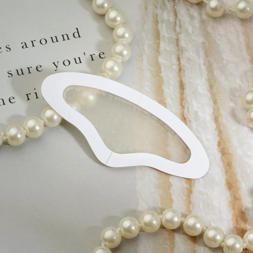 A translucent, butterfly-shaped microneedle forehead patch with a white border, resting on a background with pearls.