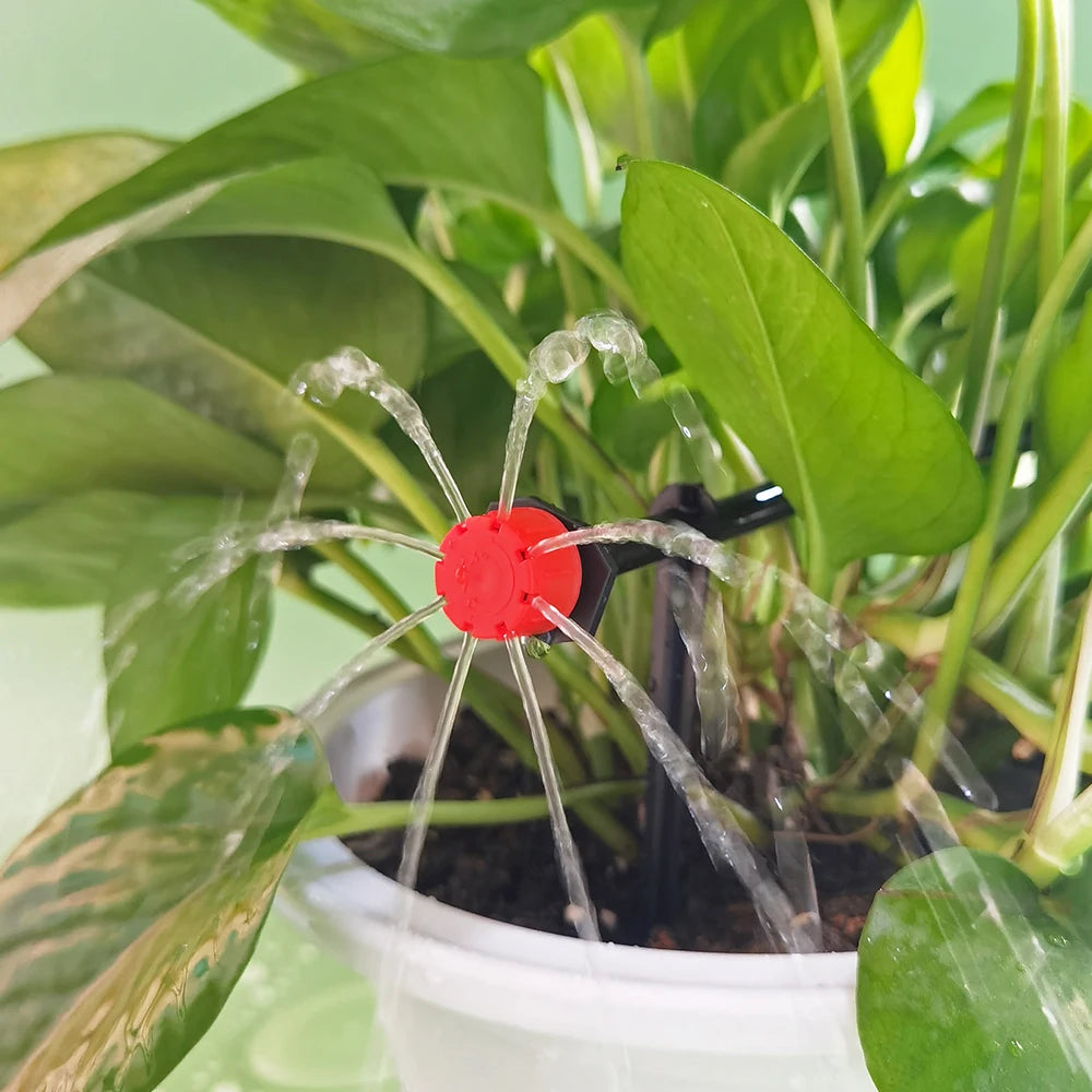 Red drip emitter watering green plant leaves from a black stake