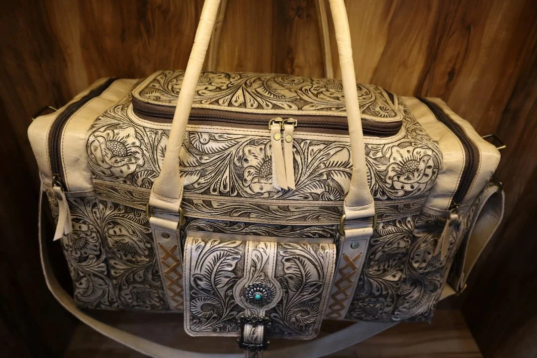 Vintage handmade brown leather travel duffel with intricate floral tooling, antique finish, and western concho detail.