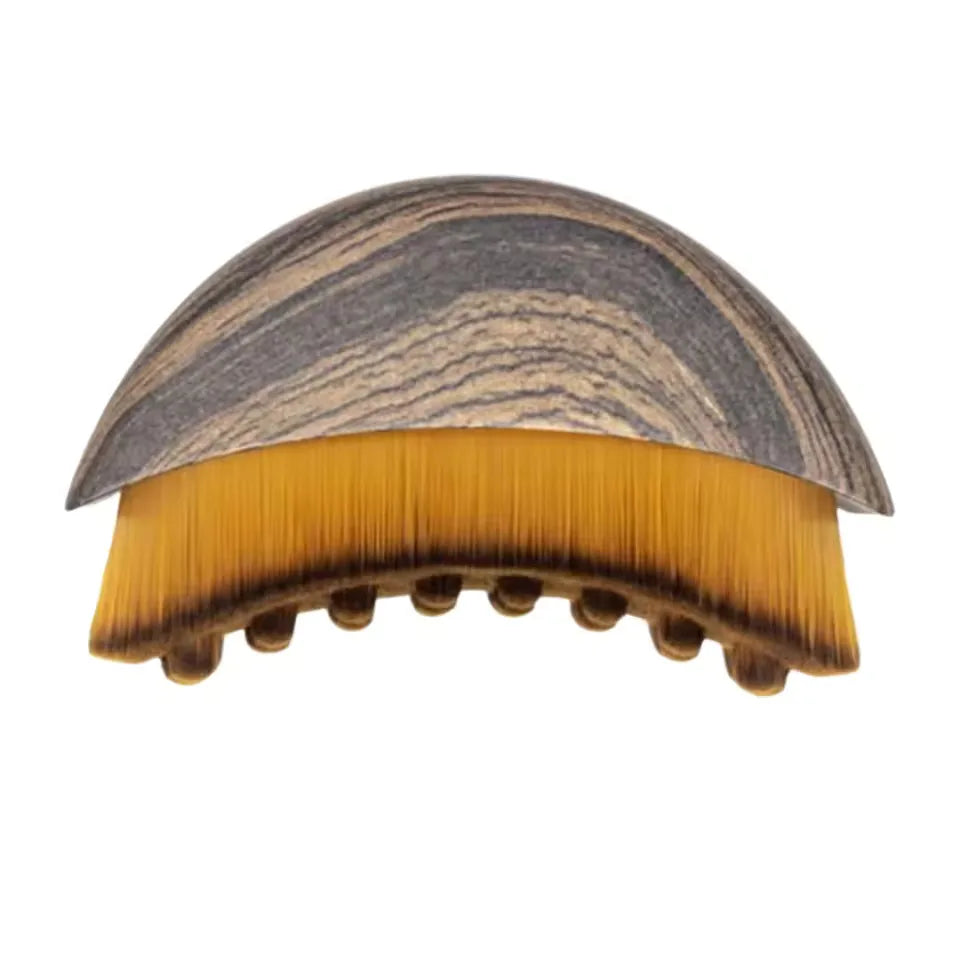 Curved, ergonomic facial brush with a grey, wood-grain top handle and soft, dense amber bristles.