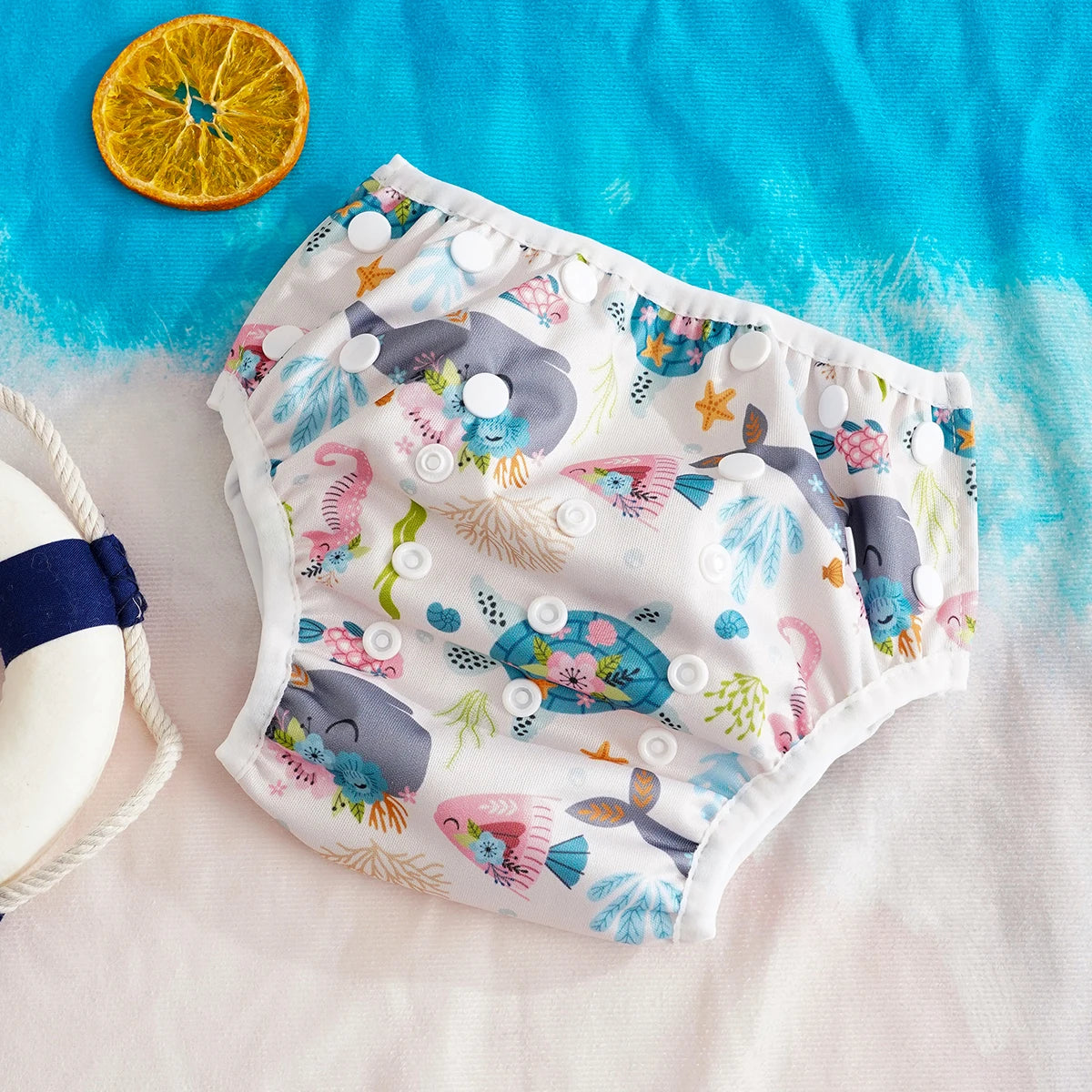 Adjustable reusable baby swim diaper with cute sea creature pattern on a beach-themed background.