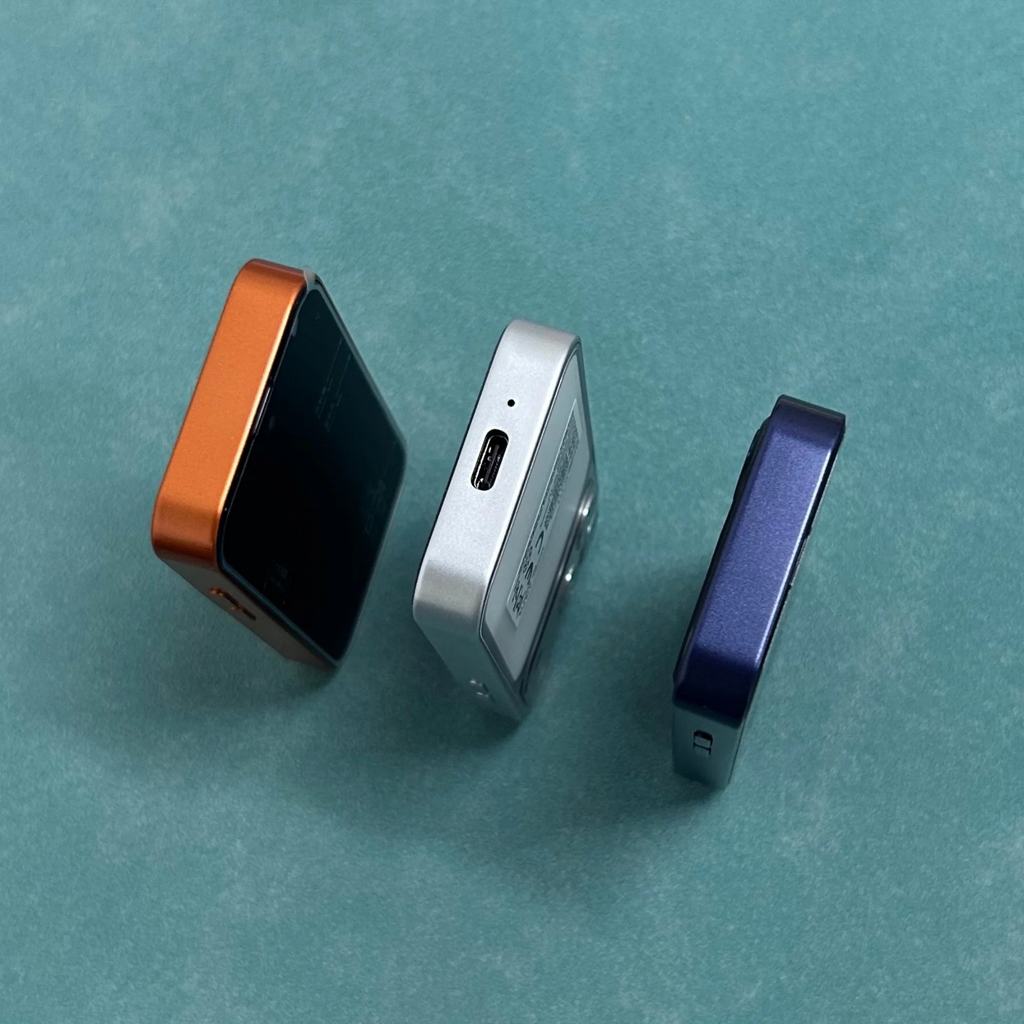 ONEMYTH A18 Pro 4G mini smartphones in orange, silver, and blue, showing Type-C port and side profiles on teal background.