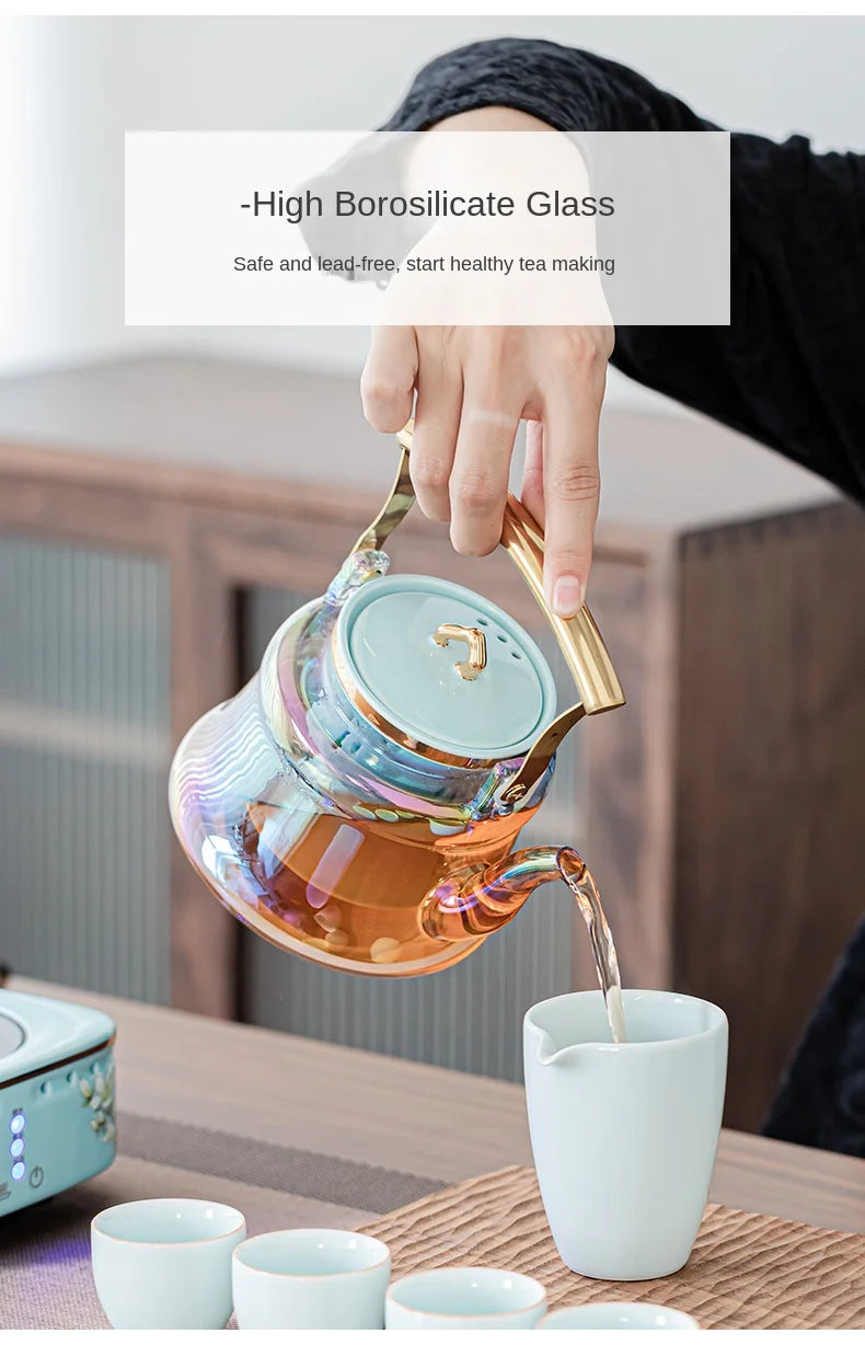 Iridescent borosilicate glass teapot with gold handle and light blue lid, pouring tea into a ceramic cup.