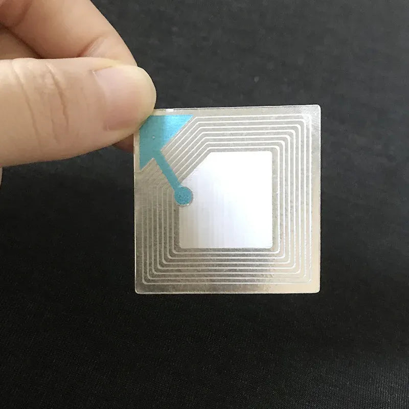RF EAS inlay anti-theft label square with antenna circuit, held between fingers