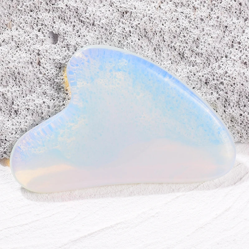 Heart-shaped opalite gua sha facial massage tool resting on a textured gray stone surface.