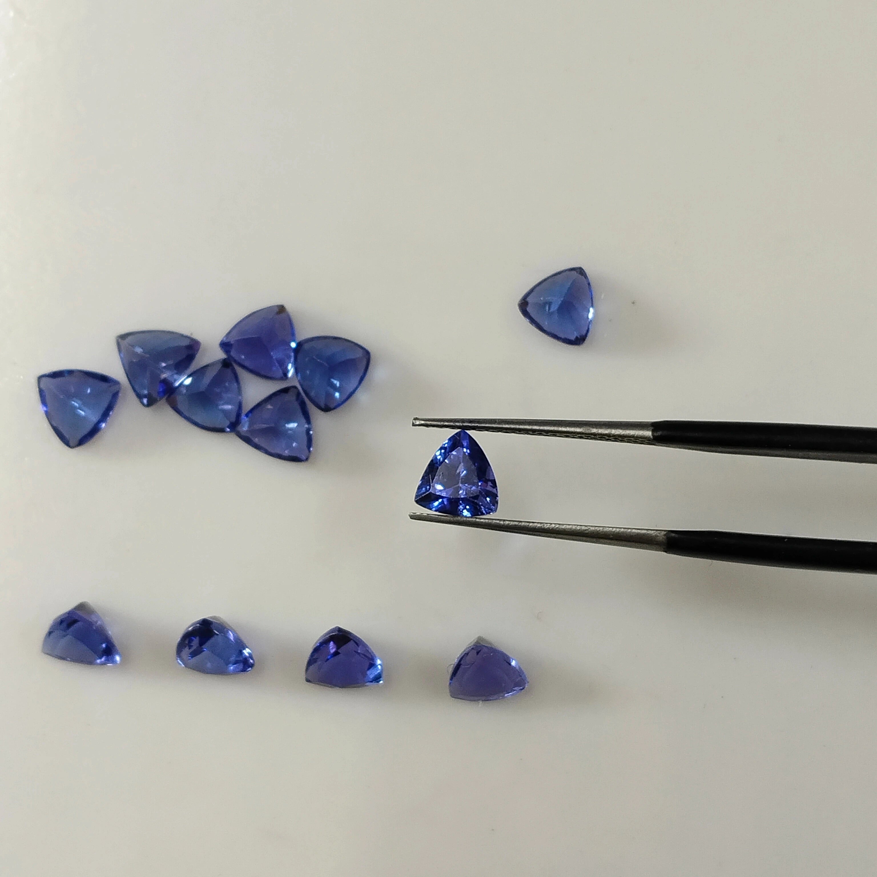 Assorted loose blue trillion-cut gemstones, scattered around tweezers