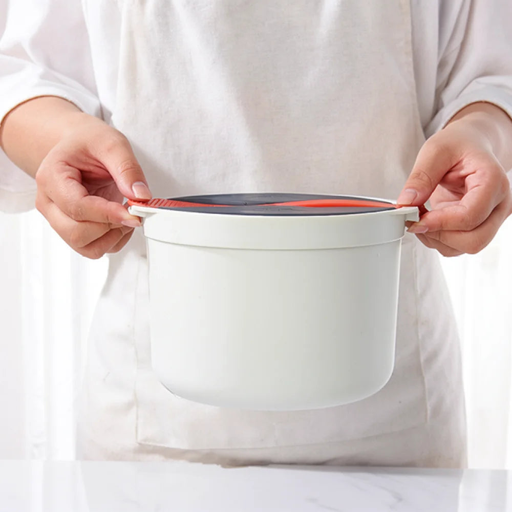 Microwave rice cooker steamer pot with lid, held by hands showing gray top and orange stripe