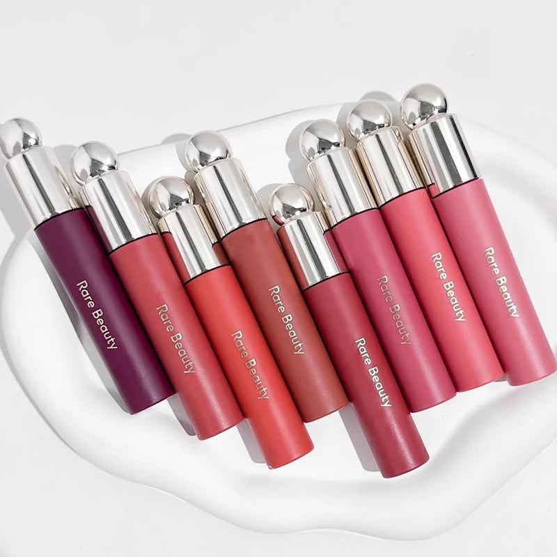 Rare Beauty Soft Pinch Tinted Lip Oil collection in various shades on a white tray, offering a long-lasting glossy stain.