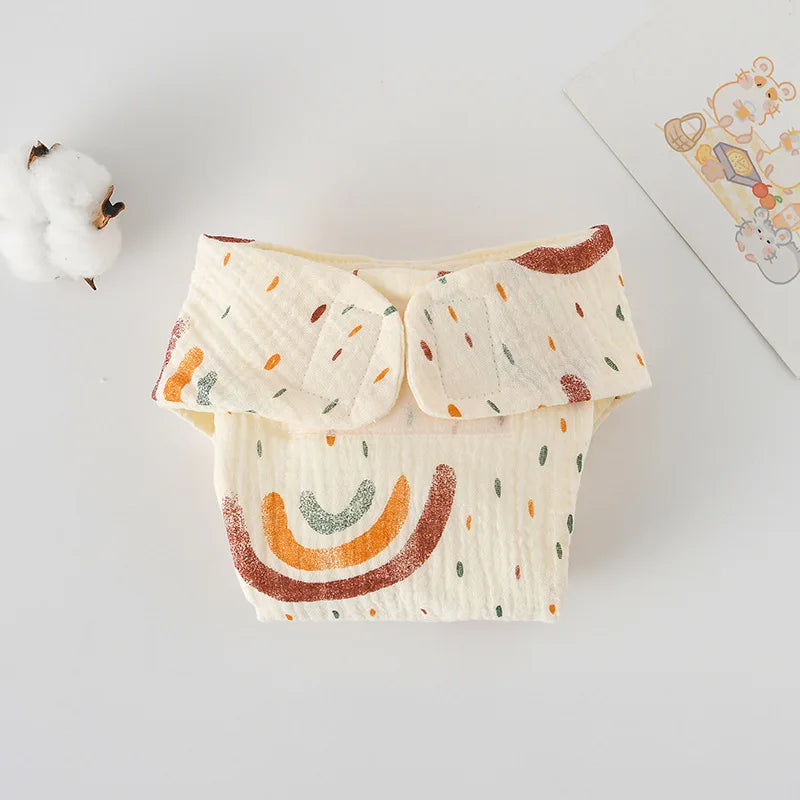 Baby care cloth diaper with cream fabric, rainbow pattern, and adjustable Velcro tabs for infants.