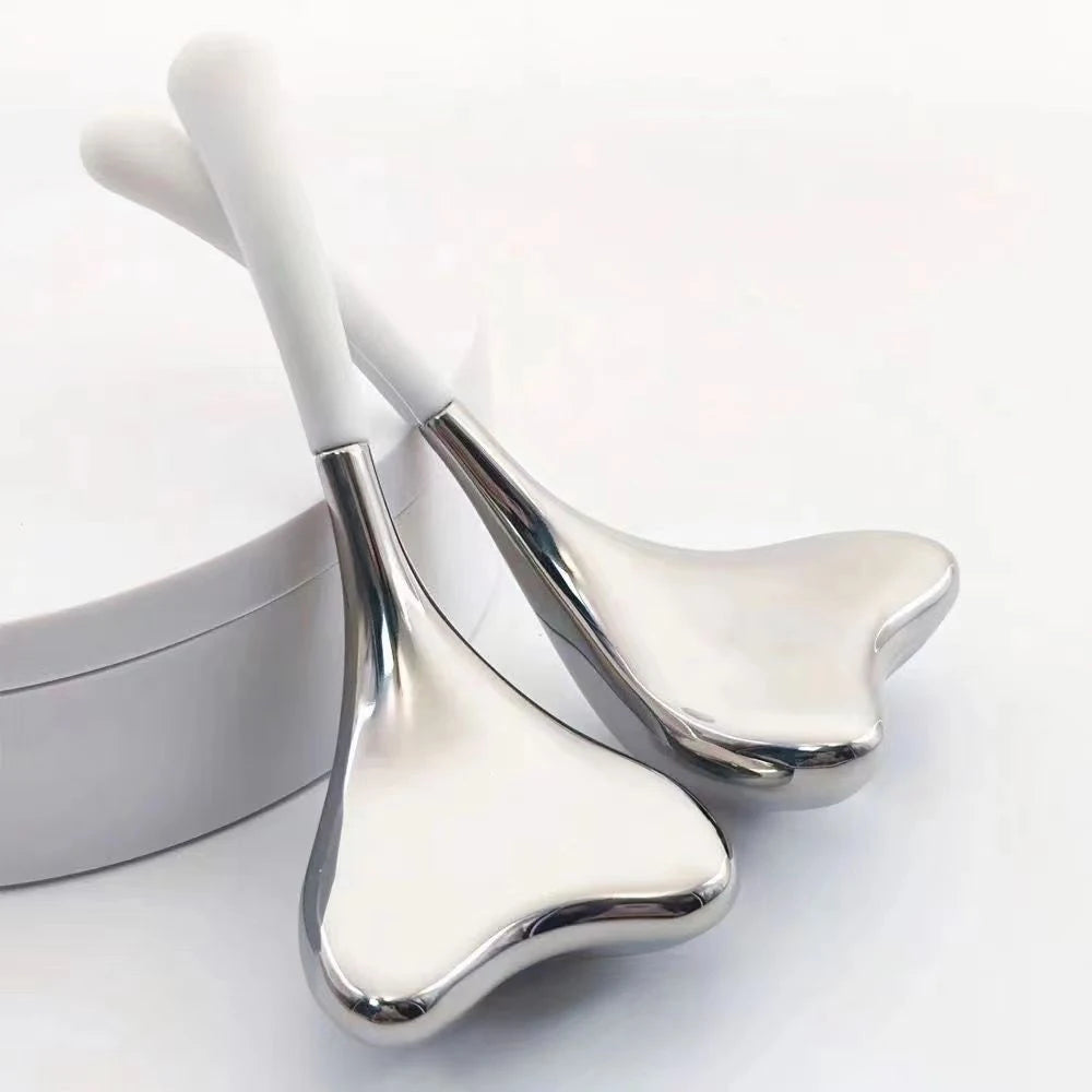 Two heart-shaped, stainless steel cryo sticks with white handles for facial massage on a white surface.