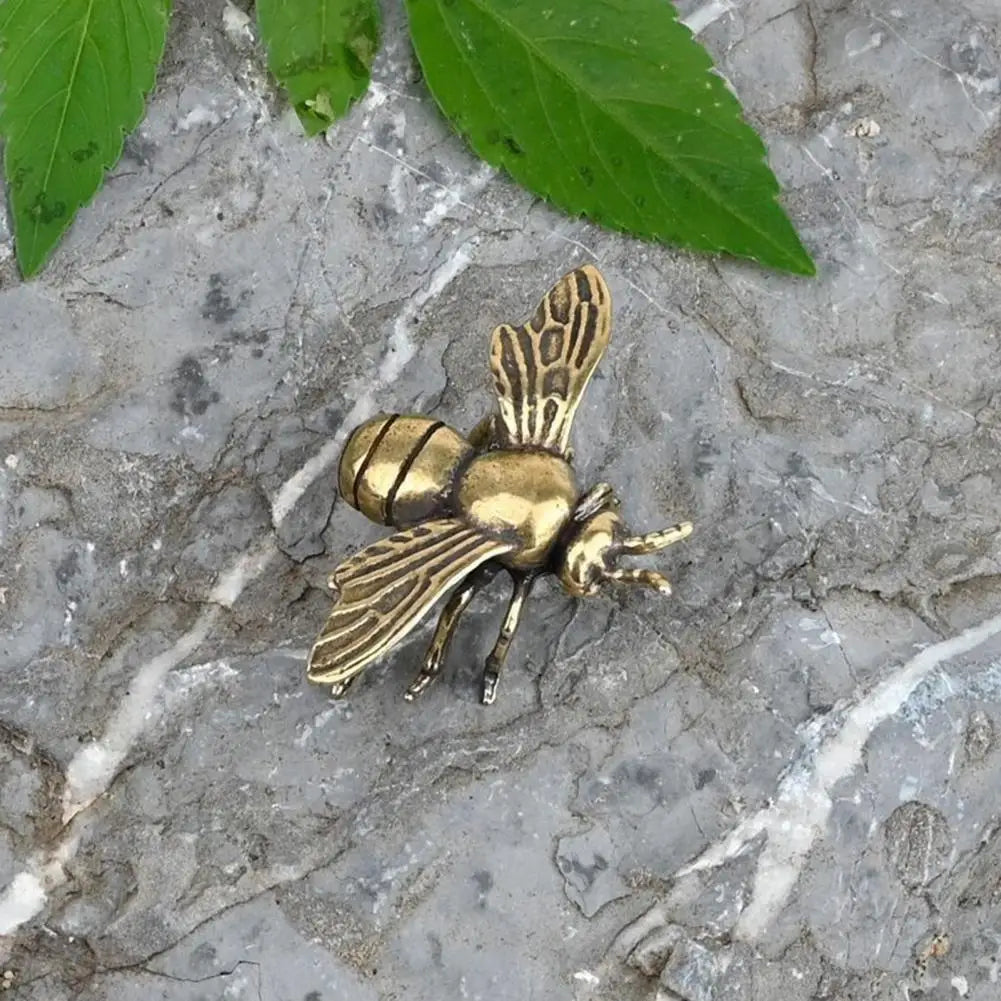 Small golden brass bee tea pet figurine for elegant desktop decor, realistic metal sculpture on grey stone background.