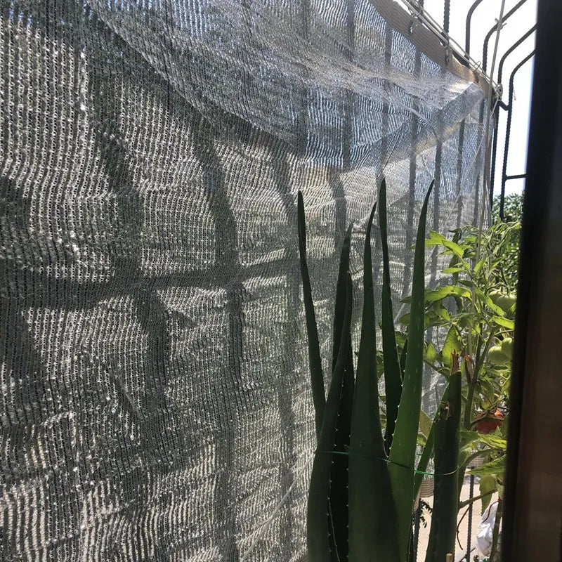Aluminum foil sunshade net screen draped over a garden fence, gray reflective mesh