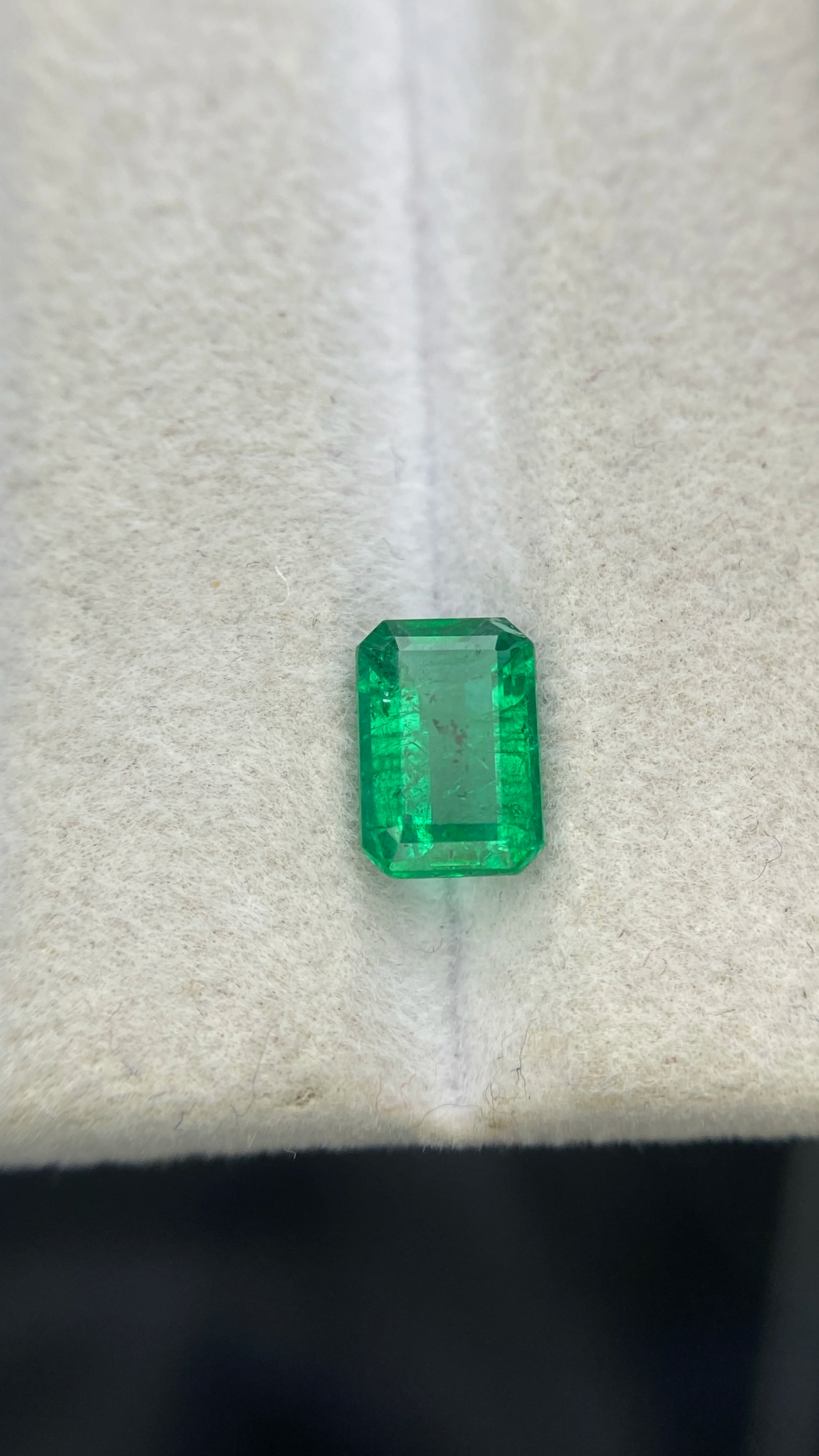 Green emerald-cut rectangular gemstone, loose faceted stone centered on white padding