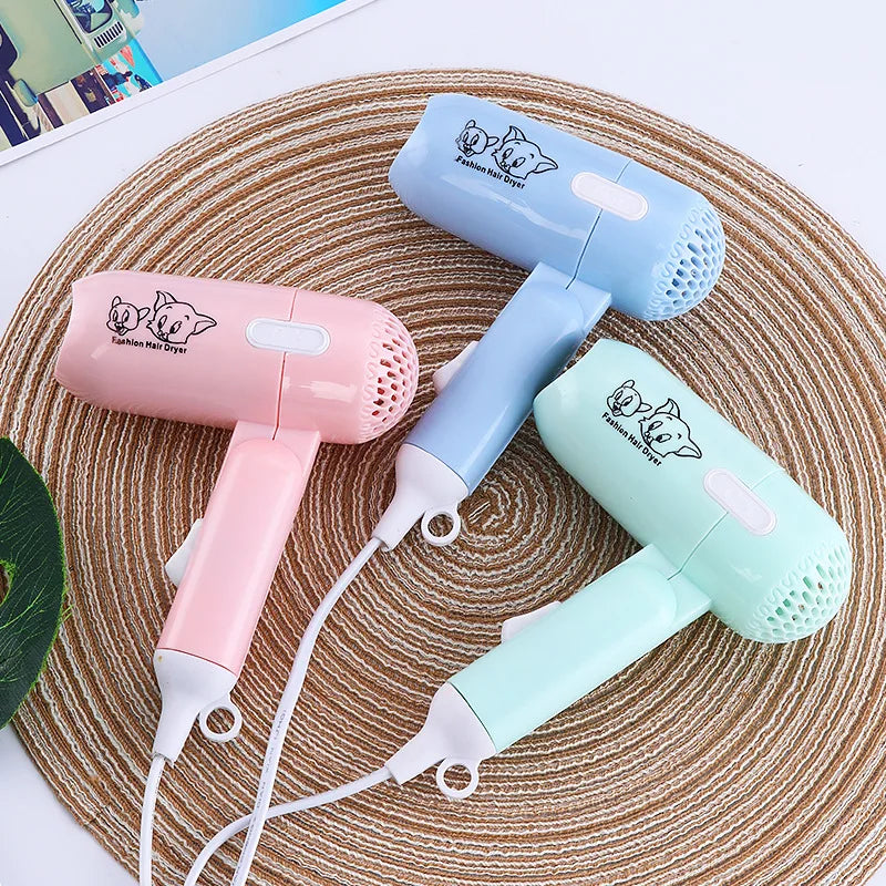 Mini folding travel hair dryers in pastel pink, blue, and green with cute cartoon design and hanging loop. 400W power.