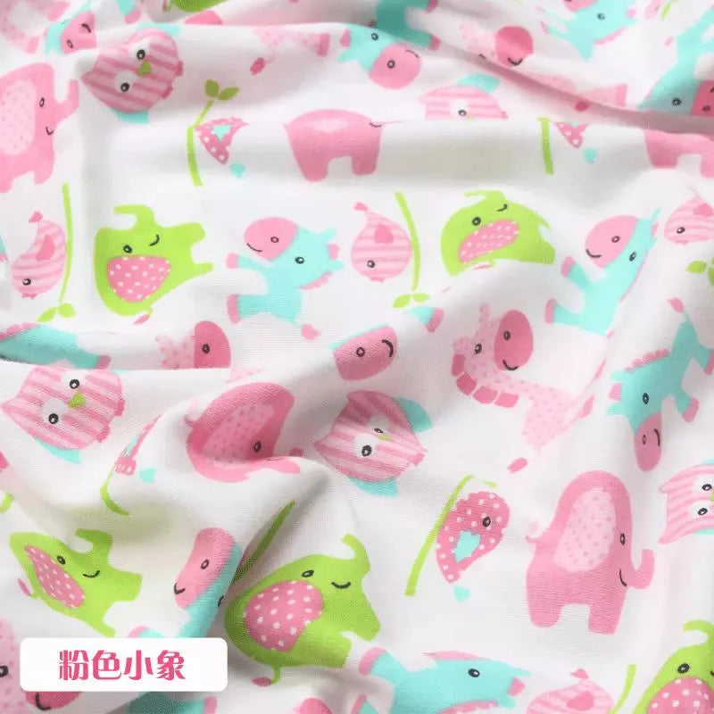 Soft white organic knit jersey fabric with a playful pink, green, and blue animal print for children's garments.