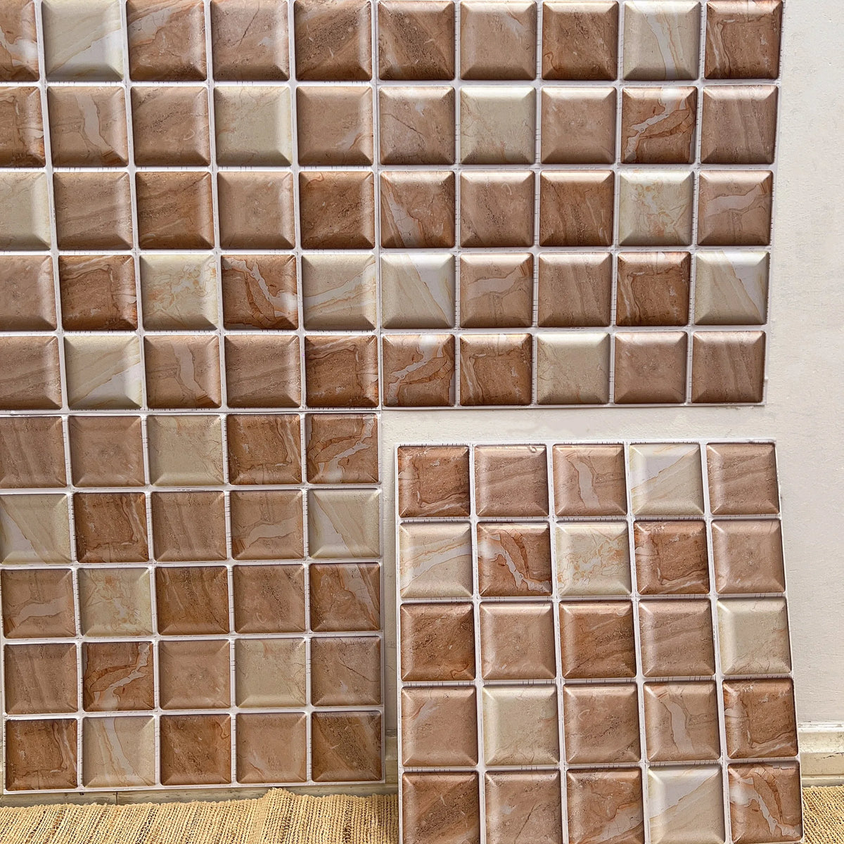 Peel-and-stick backsplash tiles with tan and cream marble-look square mosaic grid