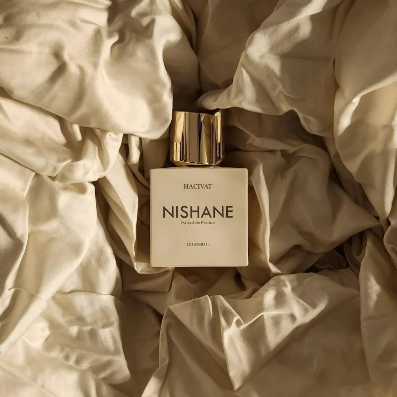 Nishane Hacivat Extrait de Parfum for men, 100ml, luxury square bottle with gold cap on cream fabric background.