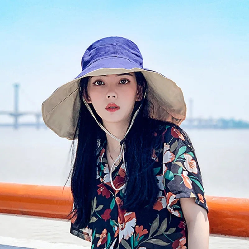 Woman wearing a Tidesmit reversible wide-brim sun hat with blue top and beige underside, featuring an adjustable chin cord.