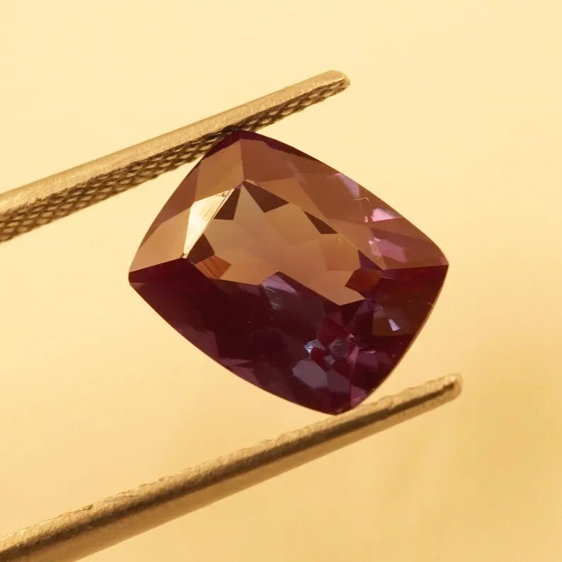 Faceted cushion-cut alexandrite gemstone, deep maroon with golden amber and red tones