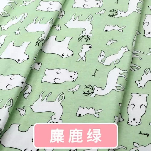 Light green cotton jersey fabric featuring a repeating white woodland animal print including deer, bears, and birds.