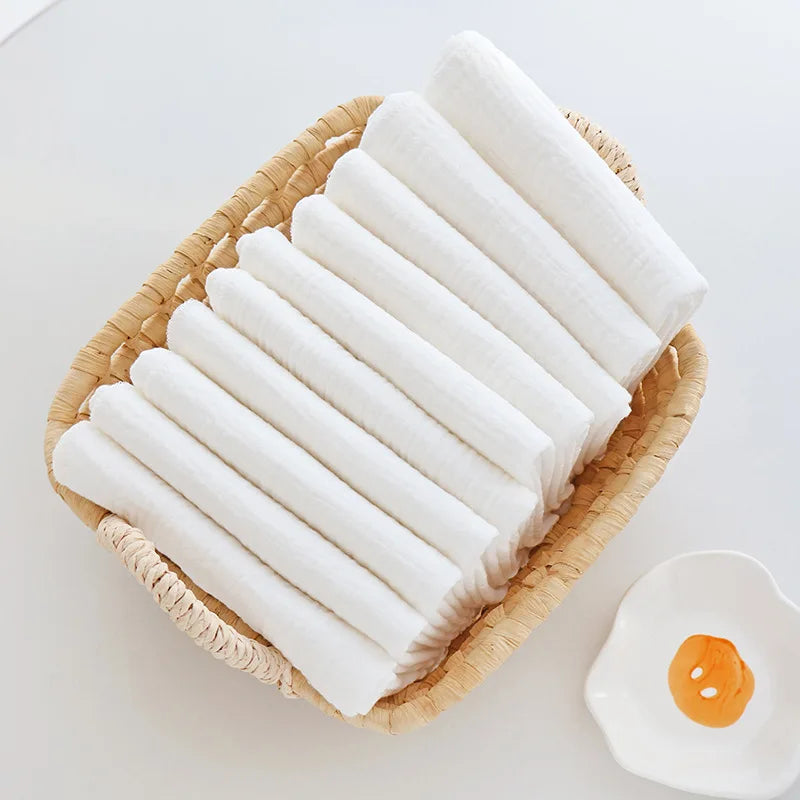 Set of soft white baby care muslin cloths folded in a woven basket. Essential baby skin care accessories.
