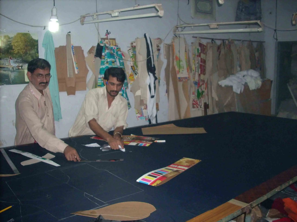 Tailors cutting dark navy fabric on a large workshop table to craft luxury leather business trunks and briefcases.